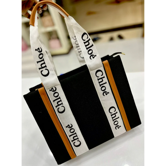 Black canvas tote bag with tan accents and white Chloé logo handles on display at Bagwati