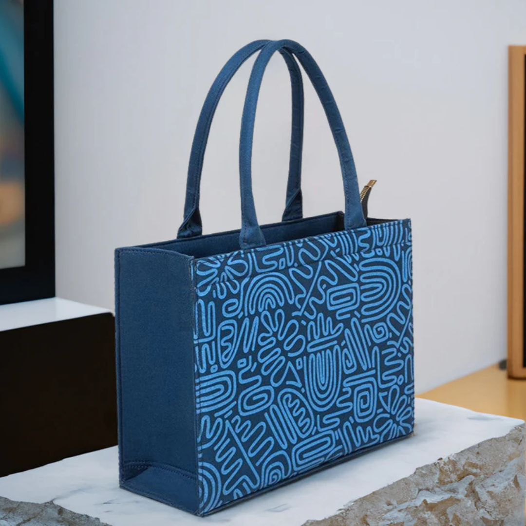Blue canvas tote bag with doodle art design by Bagwati, displayed on a marble surface