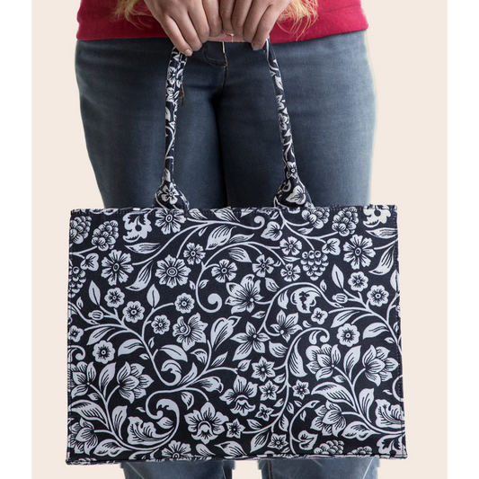 Bagwati black canvas tote bag with white floral print, held in hand, premium handbag