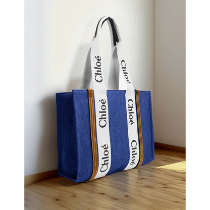 Blue canvas tote bag with white branded straps, premium design, on wooden floor