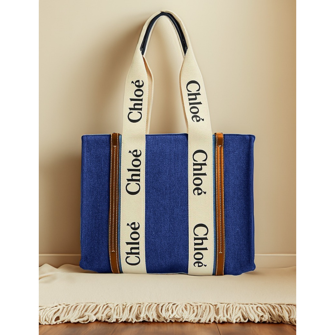 Blue canvas tote bag with cream logo handles, displayed on a beige fringed cloth, Bagwati
