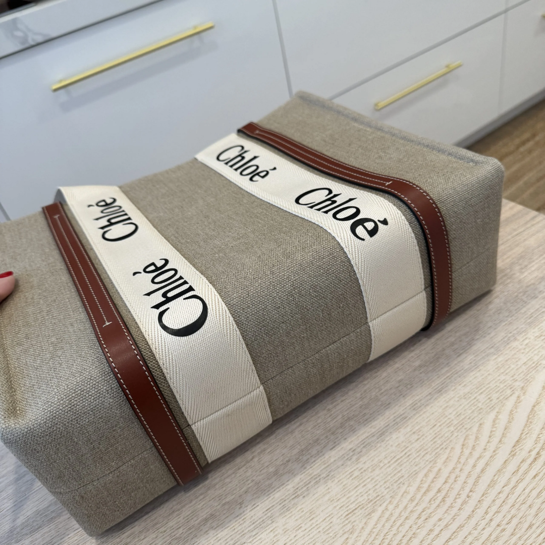 Grey canvas tote bag with brown leather trim and Chloé logo, on a wooden surface