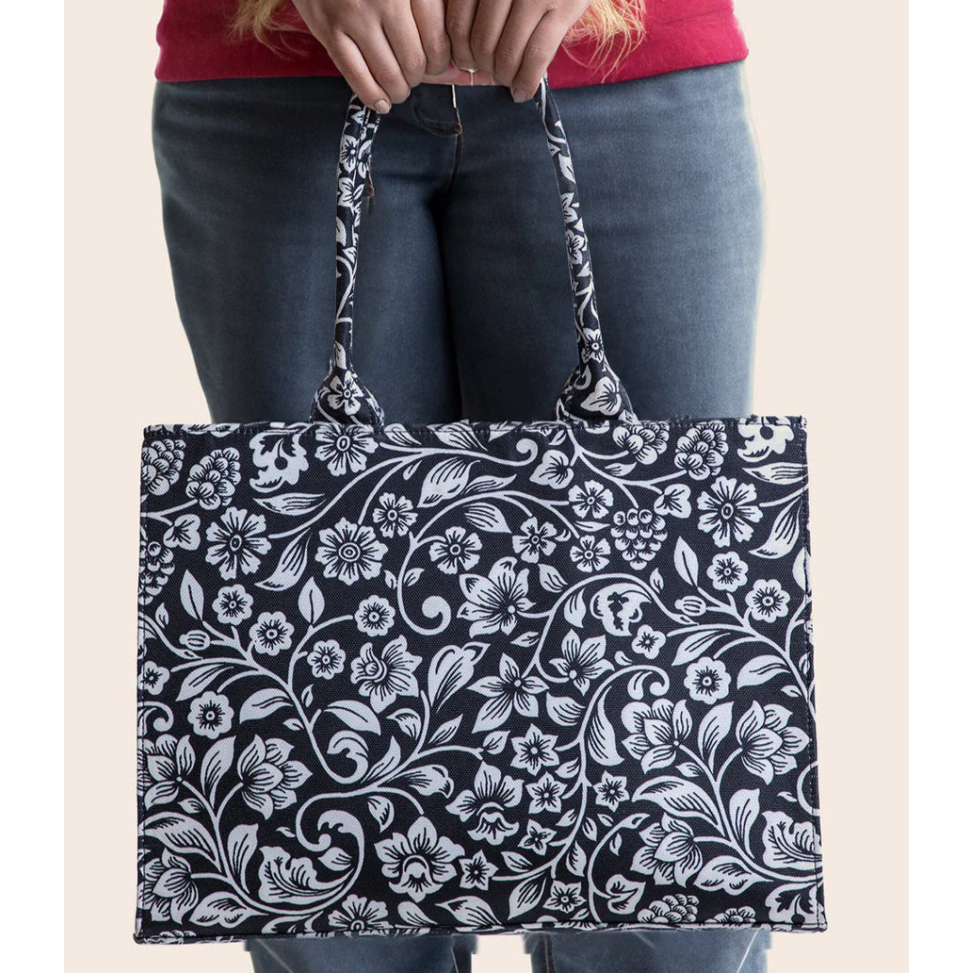 Bagwati black canvas tote bag with white floral print, held in hand, premium handbag