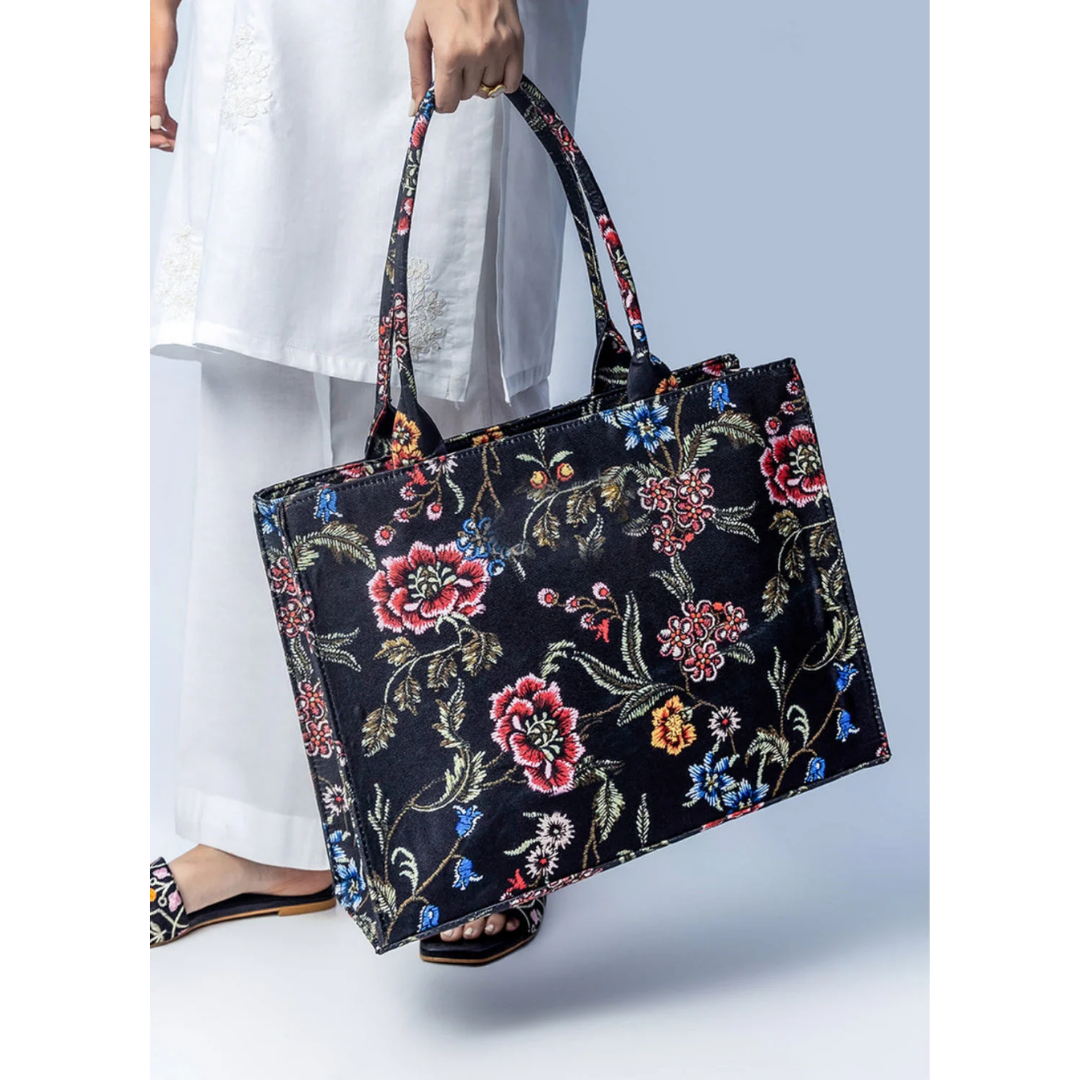 Bagwati black canvas tote bag with vibrant floral print, shown with white outfit