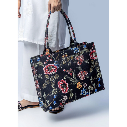 Bagwati black canvas tote bag with vibrant floral print, shown with white outfit