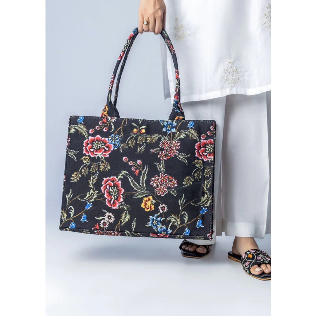 Bagwati black canvas tote bag with multicolor floral design, held by woman in white outfit.